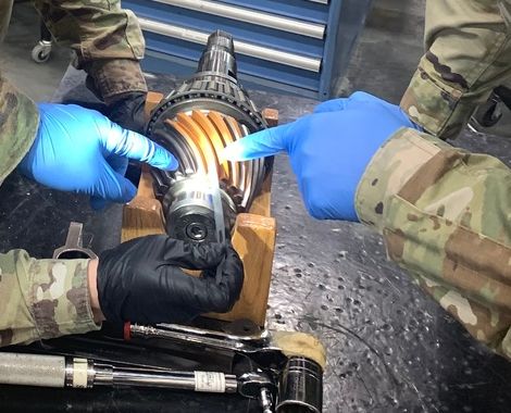 Gloved hands pointing to the gear teeth of an aviation drive component during a depot inspection